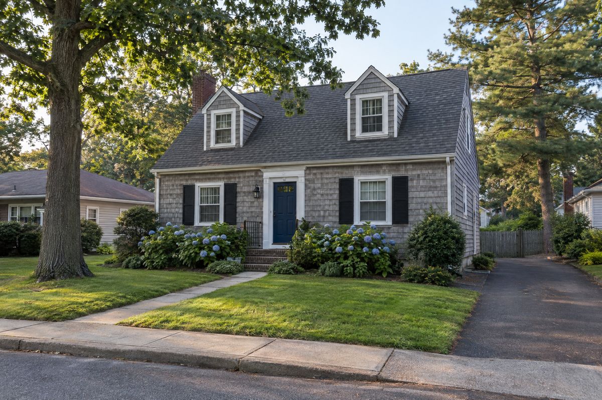 Cape Cod style house with gray cedar shake siding and a navy front door on a Suffolk County street