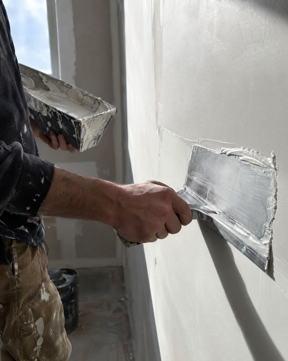 Hands using a trowel to skim coat a sheetrock wall smooth