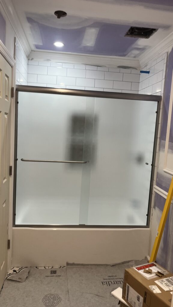 Bathroom tub with white subway tile walls and a new sliding glass door