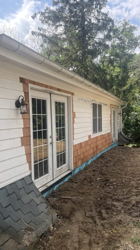 House wall with new cedar shingles going up around a set of French doors
