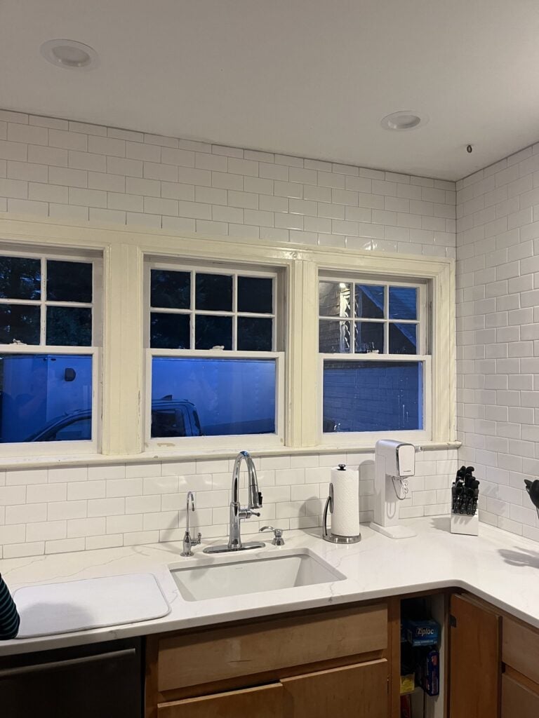 Finished white subway tile backsplash around three kitchen windows and the sink