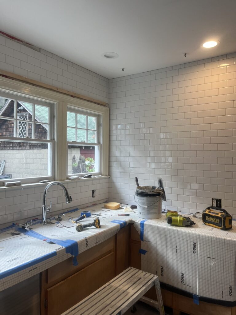 Kitchen backsplash half tiled in white subway tile, counters taped and protected